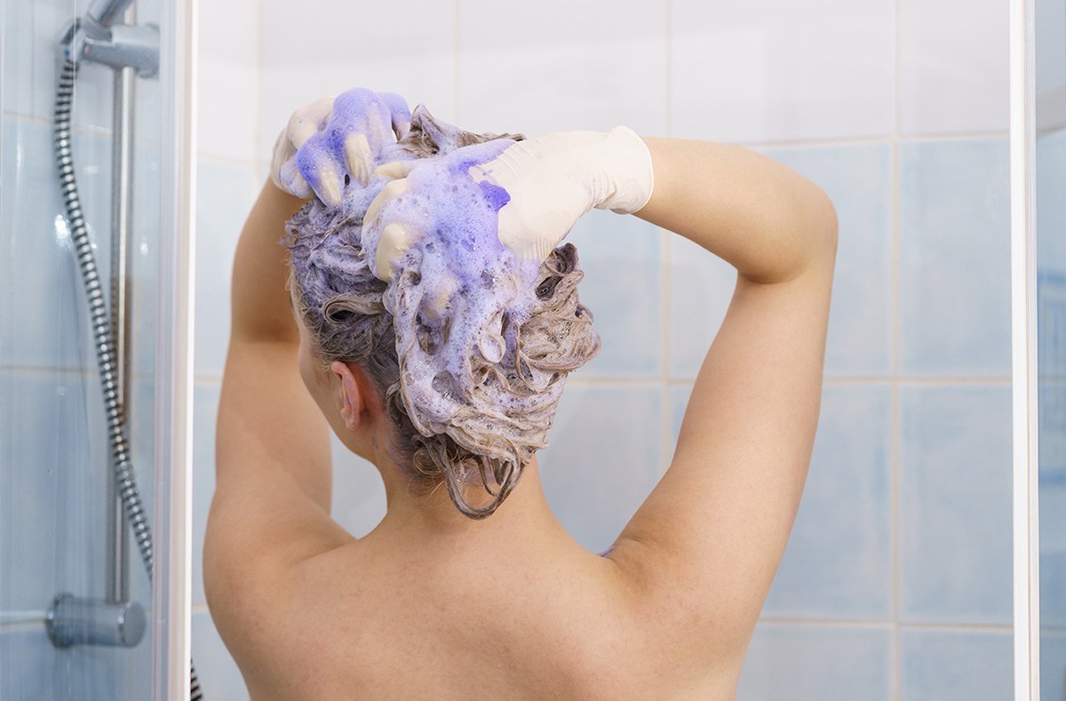 A person washing their hair in the shower with purple shampoo