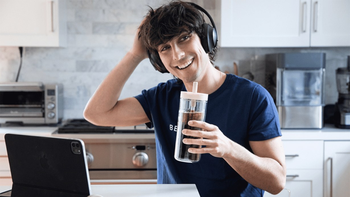 A young smiling man drinking coffee and using Bose Headphones 700 A young smiling man drinking coffee and using Bose Headphones 700
