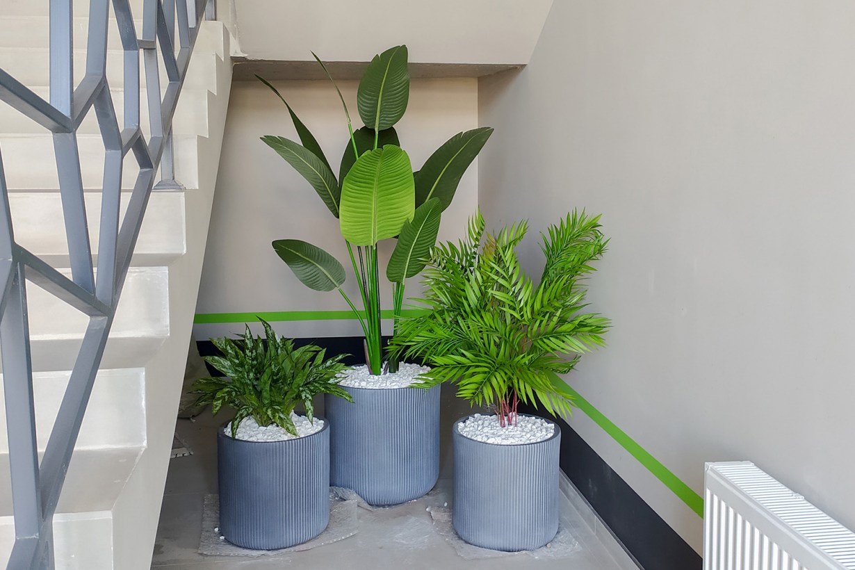three artificial plants in pots under the stairs