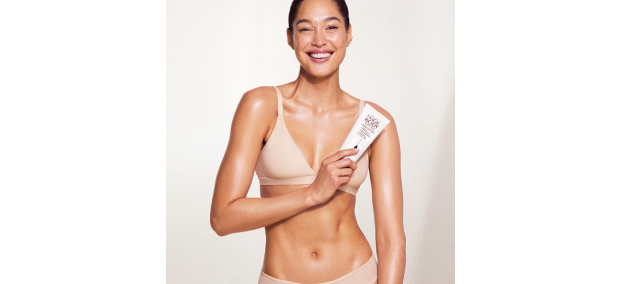 Smiling woman holding tube of Charlotte Tilbury Magic Body Cream